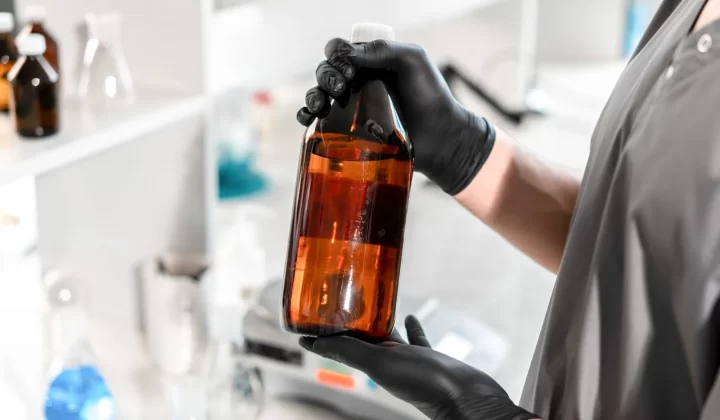实验室中戴黑手套的手持棕色玻璃瓶