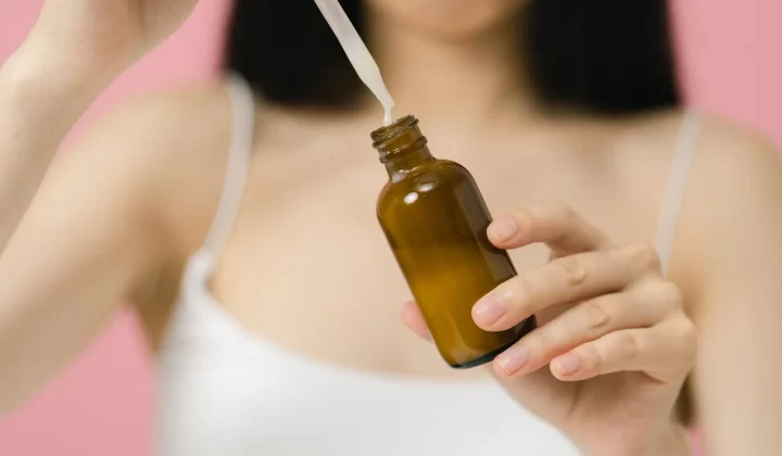 女性使用滴管精华瓶,粉色背景