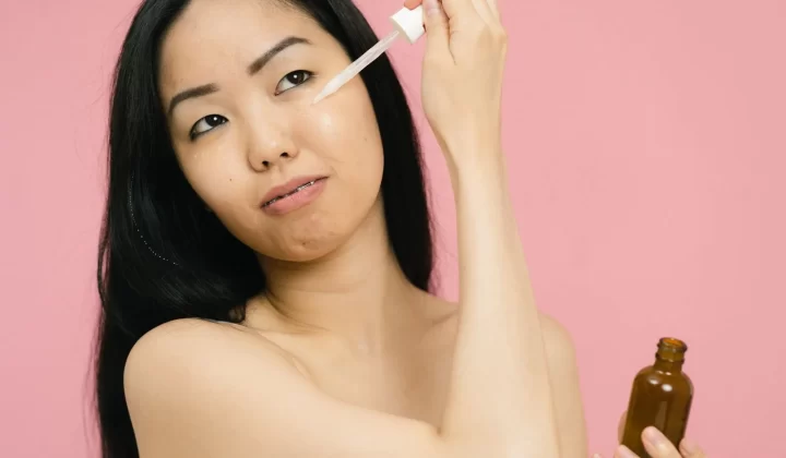 女性手持精华瓶涂抹护肤品,粉色背景