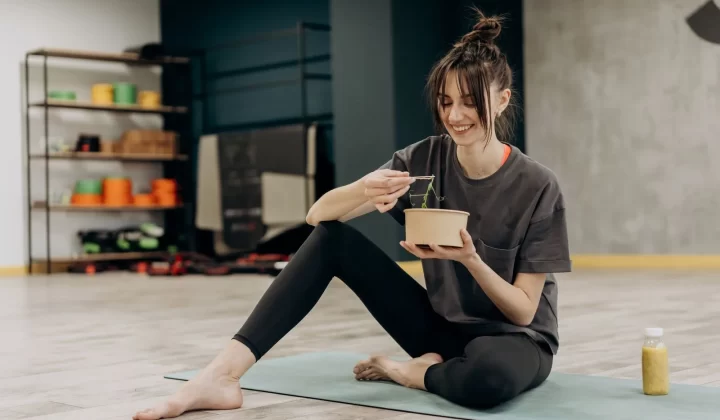 女性运动后坐在瑜伽垫上吃沙拉