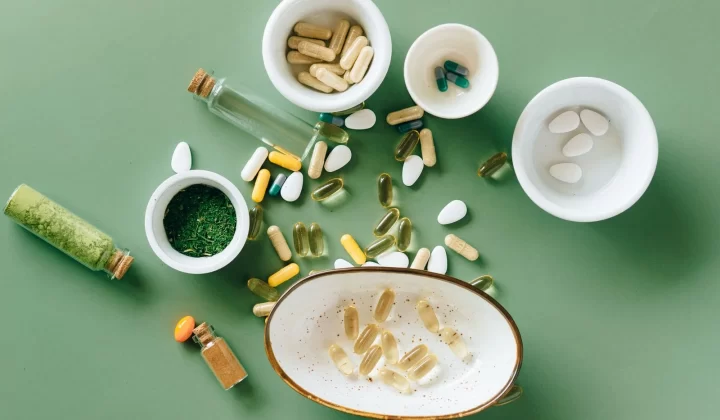 多种草本和药用补充剂放在陶瓷碗中,绿色背景俯拍