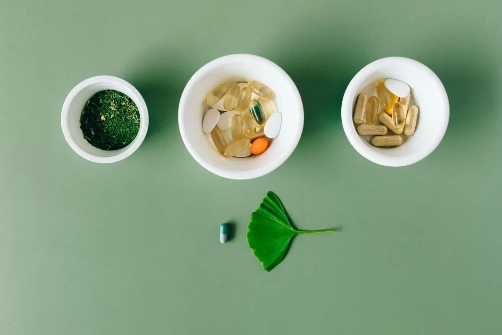 胶囊和草本药材放在陶瓷碗中,绿色背景平铺