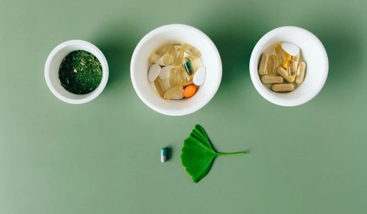 胶囊和草本药材放在陶瓷碗中,绿色背景平铺