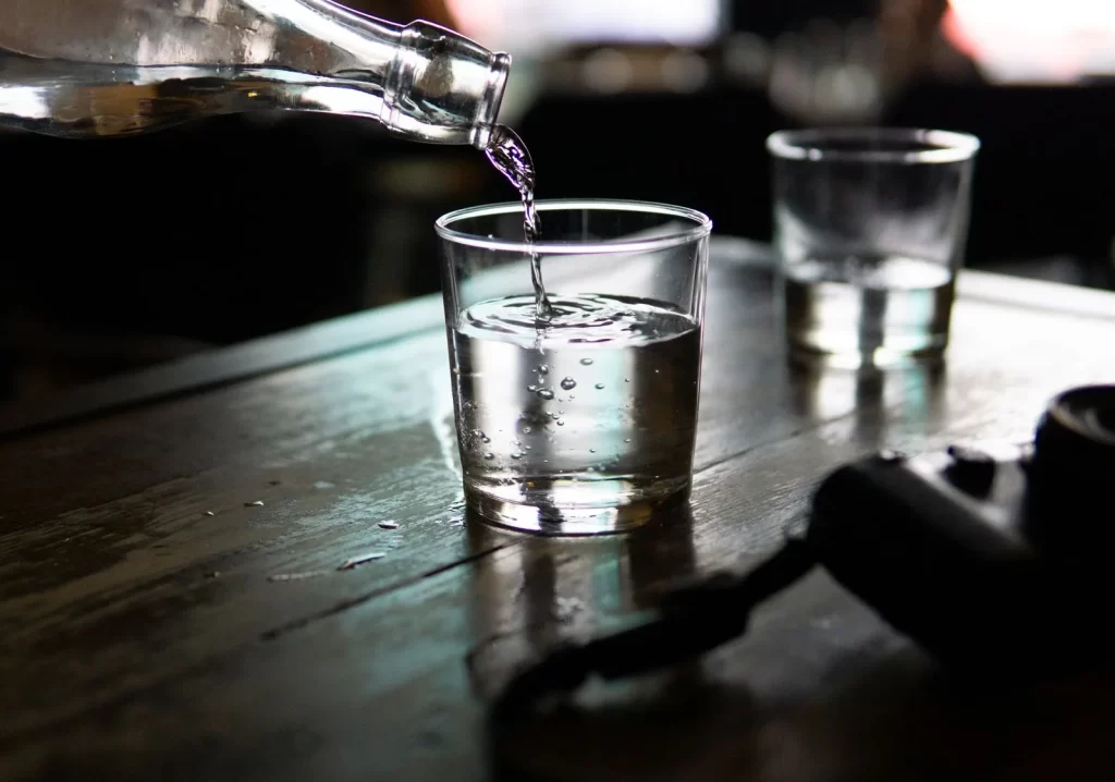 清水从瓶中倒入透明玻璃杯,木质桌面昏暗光线