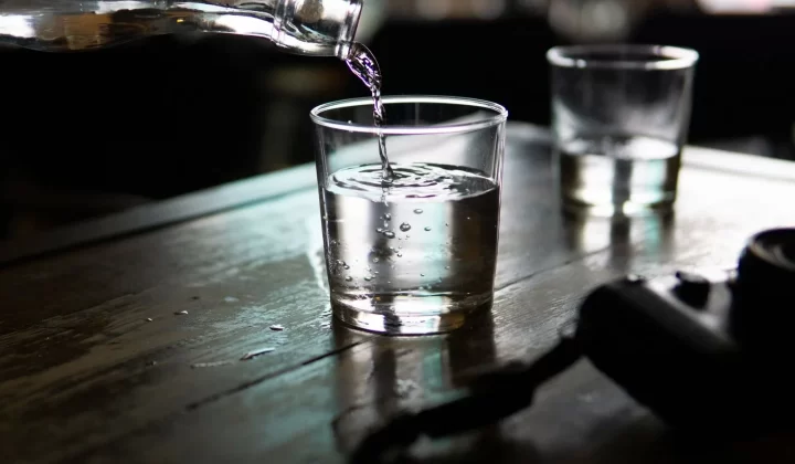 清水从瓶中倒入透明玻璃杯,木质桌面昏暗光线