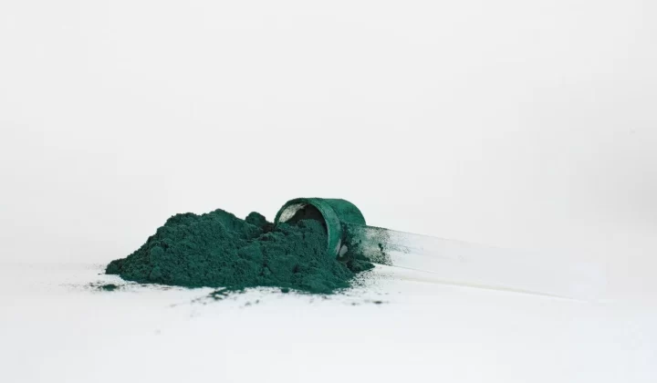 螺旋藻粉末堆放在透明量勺中,白色背景特写