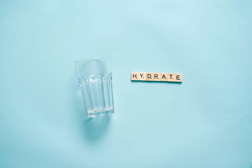 极简平铺,饮水玻璃杯搭配字母拼出HYDRATE字样,蓝色背景
