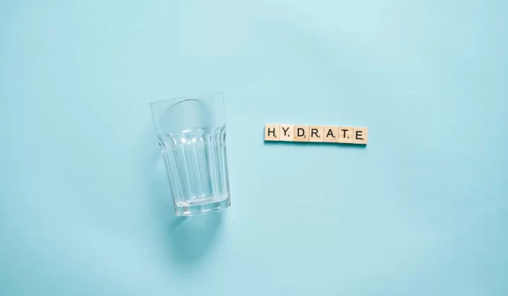 极简平铺,饮水玻璃杯搭配字母拼出HYDRATE字样,蓝色背景