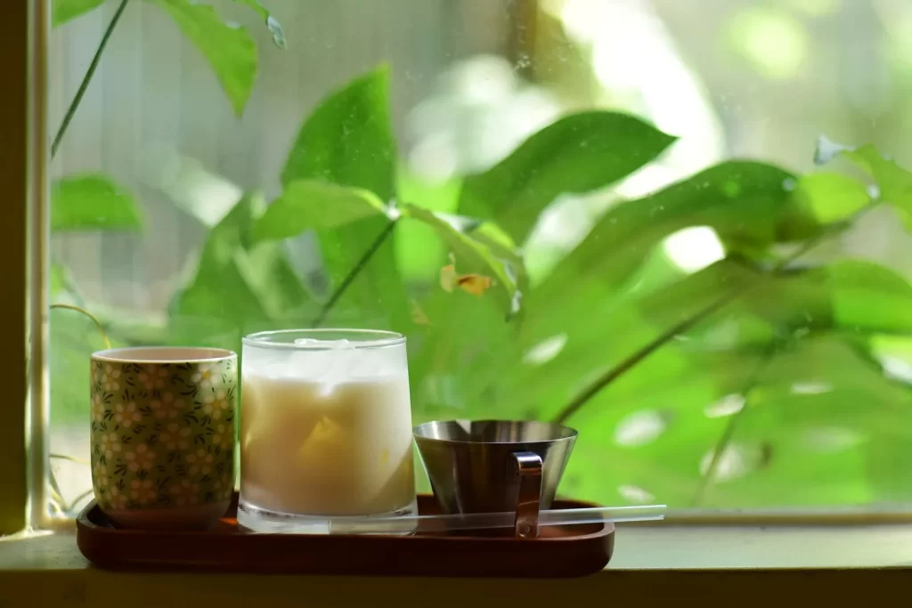 宁静场景,咖啡杯搭配一杯牛奶放在阳光洒入的窗边,翠绿背景