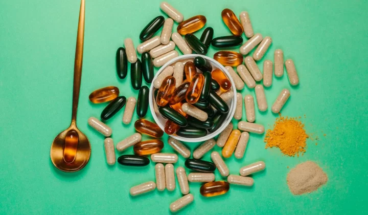 鲜艳胶囊和粉末组合放在绿色背景上,搭配金色勺子