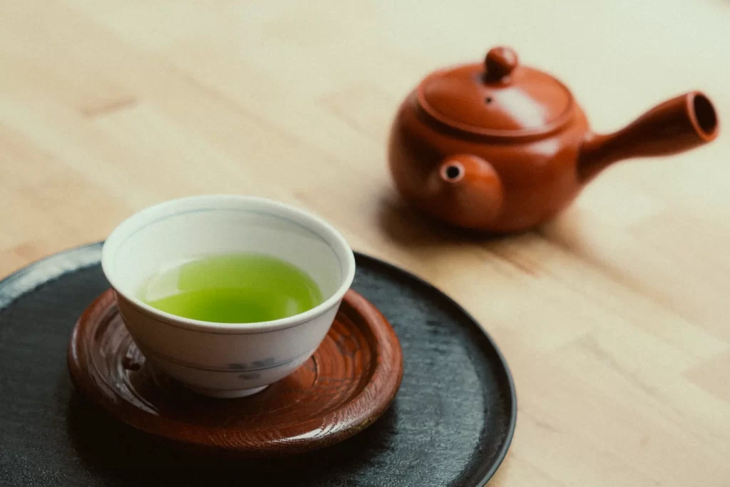 一杯鲜艳绿茶搭配陶土茶壶放在木质表面,展现宁静氛围