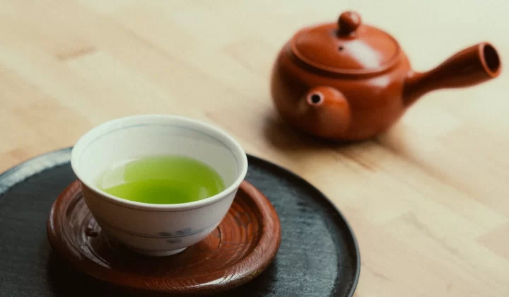 一杯鲜艳绿茶搭配陶土茶壶放在木质表面,展现宁静氛围