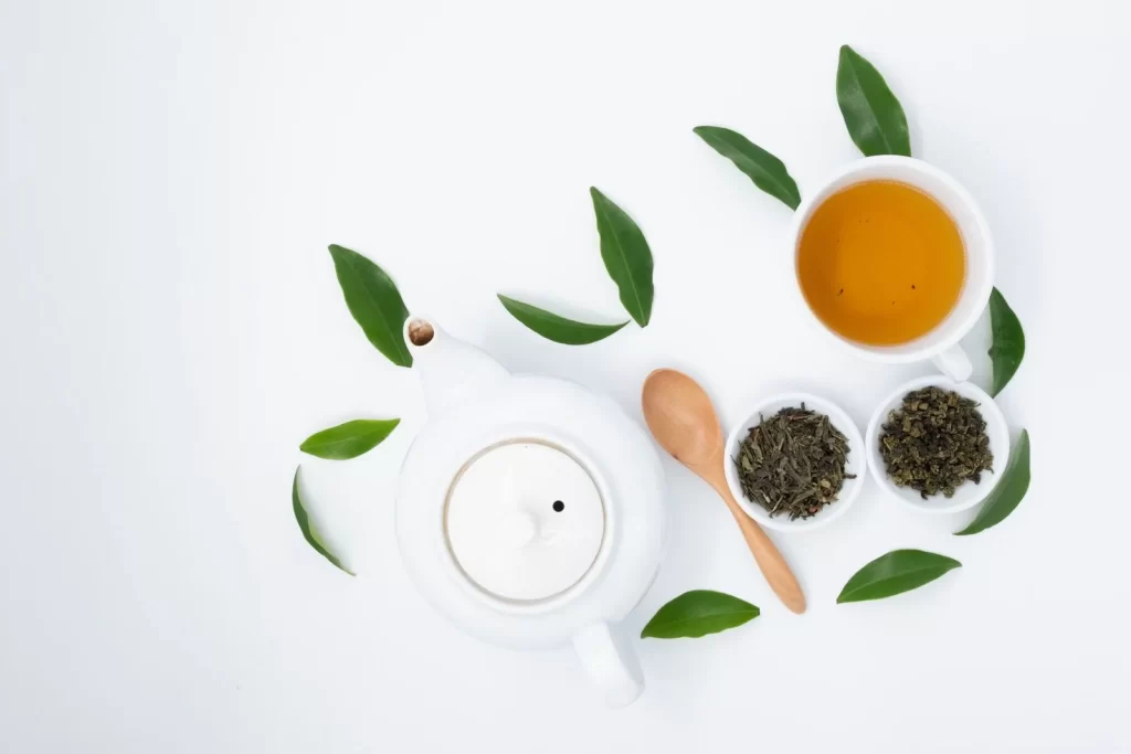 绿茶杯搭配干燥新鲜茶叶和陶瓷茶壶,俯拍白色桌面
