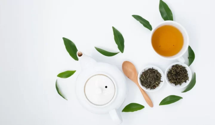 绿茶杯搭配干燥新鲜茶叶和陶瓷茶壶,俯拍白色桌面