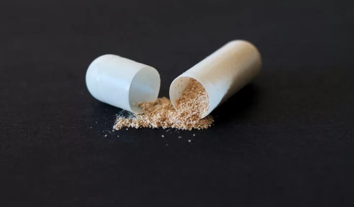 裂开的胶囊粉末洒落在深色表面,象征药物和健康