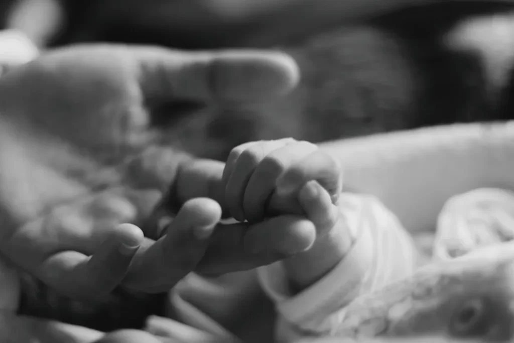 a black and white photo of a person holding a baby's hand