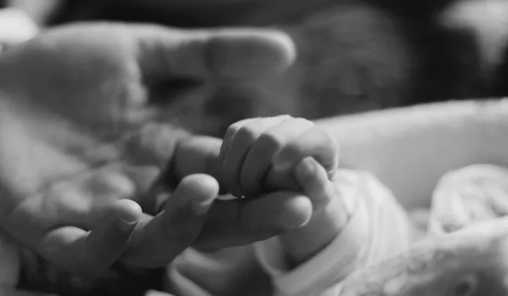 a black and white photo of a person holding a baby's hand