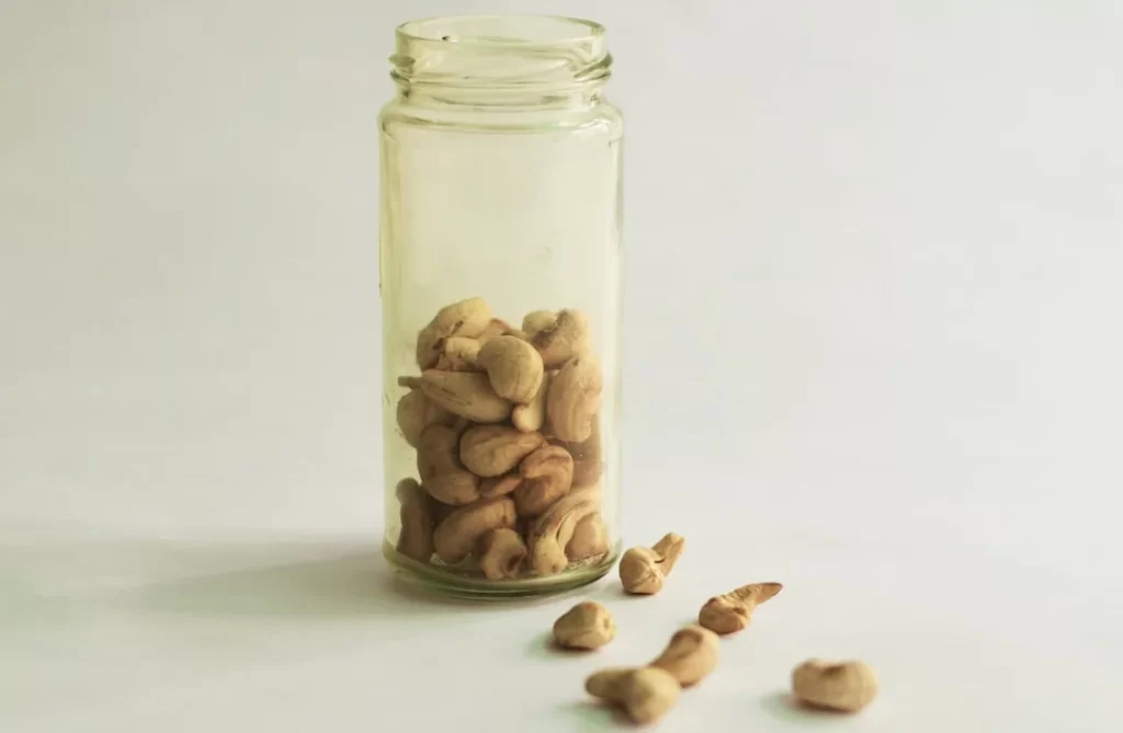 Cashew nuts in a glass jar and spilled on white.