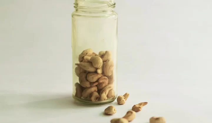 Cashew nuts in a glass jar and spilled on white.