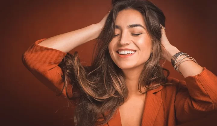 smiling woman in brown top holding hairs