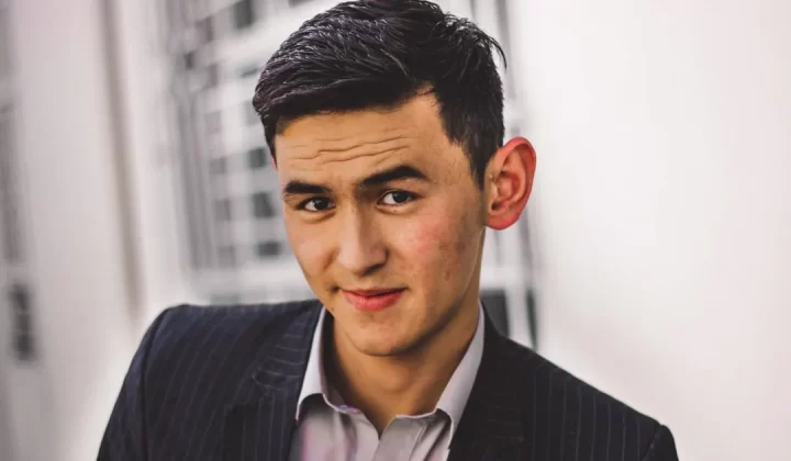 man in black blazer smiling by wall