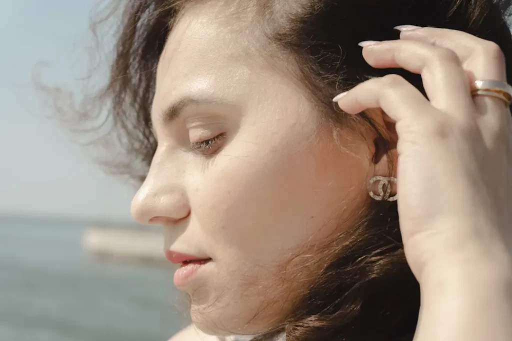 Young woman's profile with hand touching her hair outdoors.