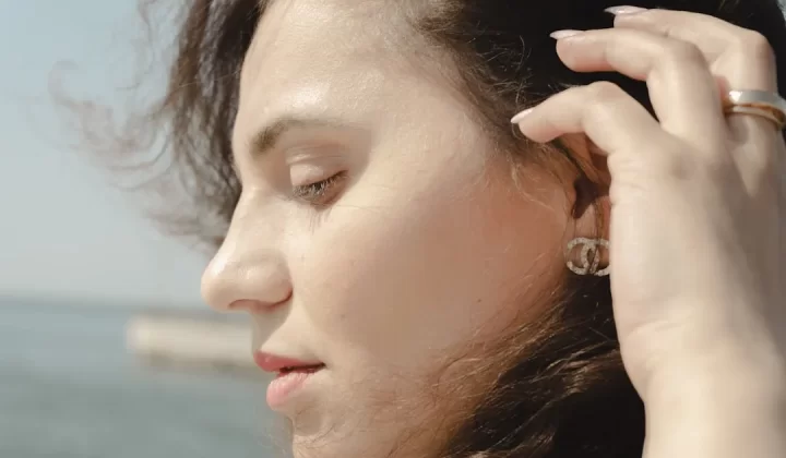 Young woman's profile with hand touching her hair outdoors.