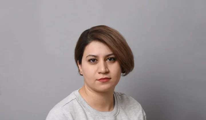 a woman in a gray shirt is posing for a picture
