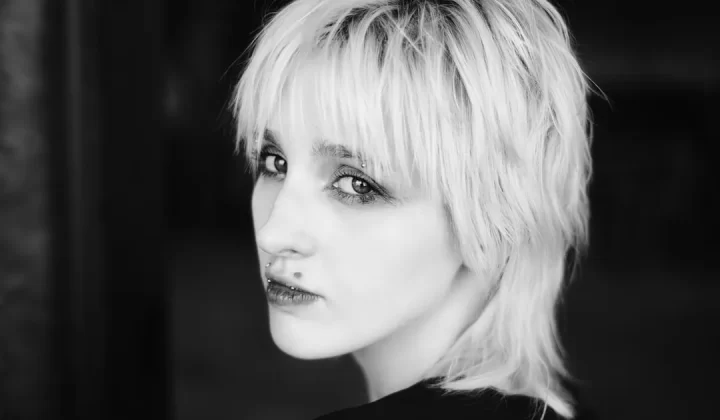 A woman with short, light hair looking over her shoulder.