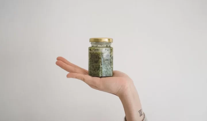 person holding green kush in glass jar