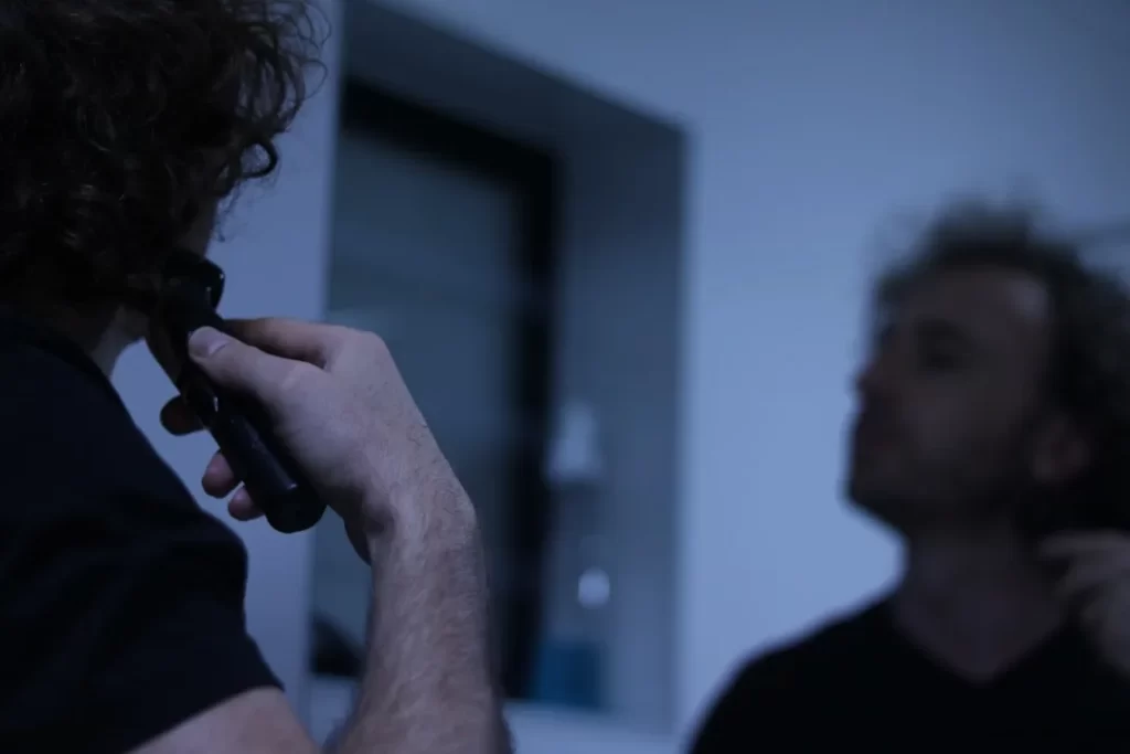 Man with curly hair shaving his neck in mirror