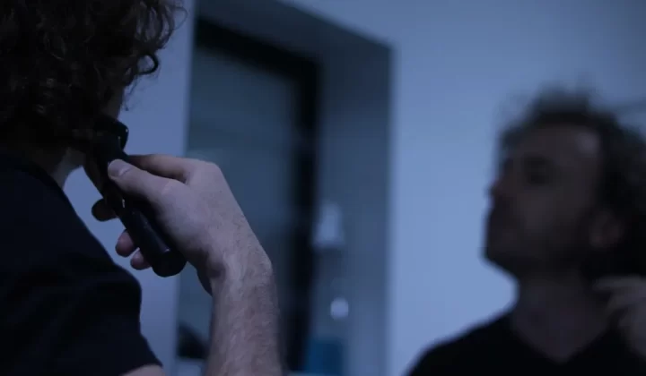 Man with curly hair shaving his neck in mirror