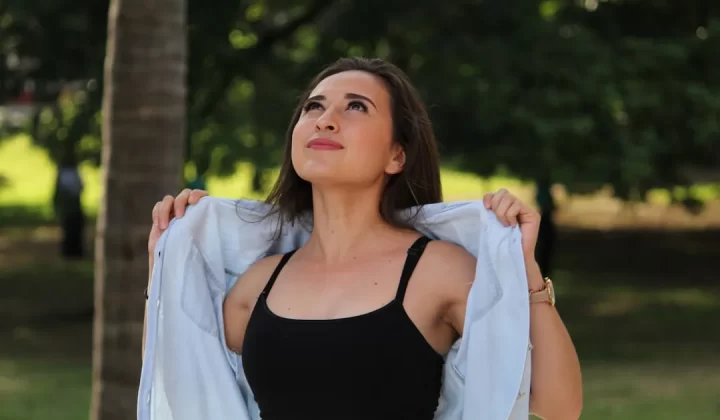 Young woman adjusting shirt while looking up in nature.