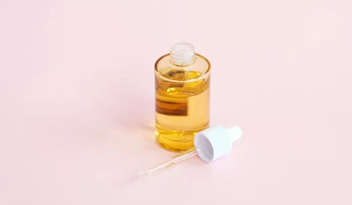 Skincare serum bottle and dropper on a pink surface.
