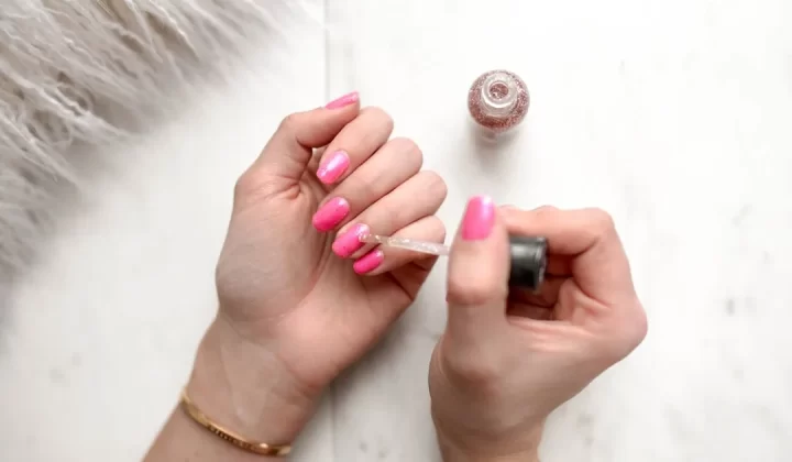 person spreading glittered nail polish on pink nails