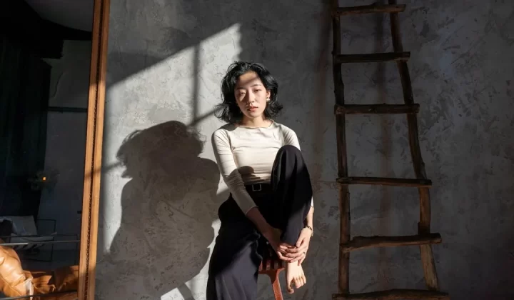 Woman sitting in a room with dramatic light and shadows.