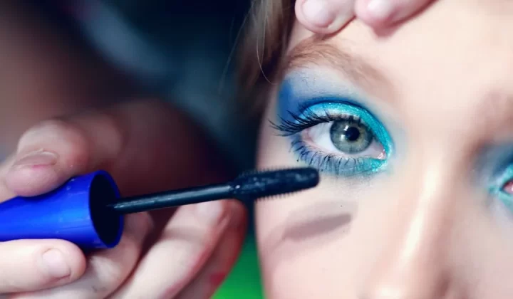 mascara being applied on woman's eyelash with blue eyeshadow