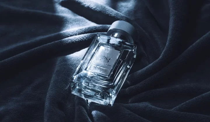 A clear glass bottle of perfume on dark fabric.