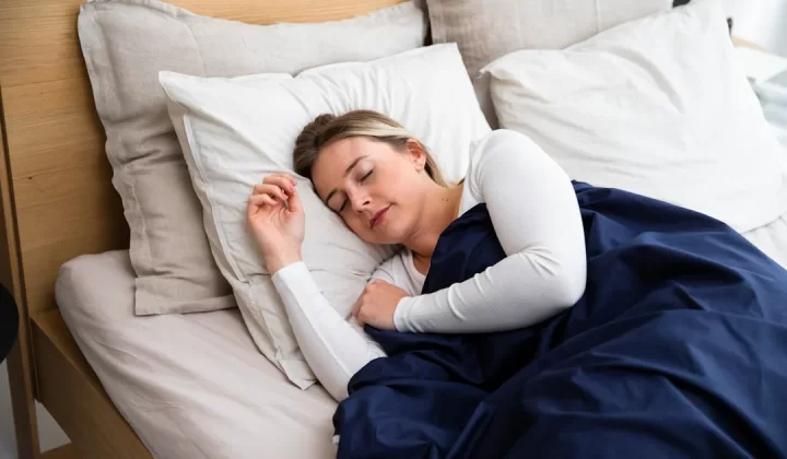 a woman sleeping on a bed with a blue blanket